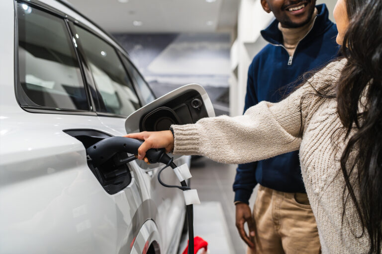 Two people looking at an electric vehicle on charge in a showroom, with one person holding the charging cable connected to the car.